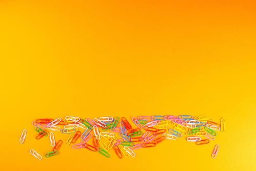 A pile of colored paper clips scattered on a orange surface.