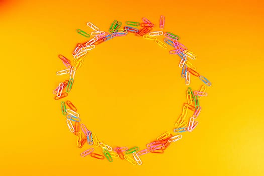 Pile of colored paper clips arranged in a circle on an orange surface.
