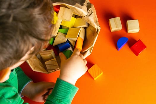 A child plays with wood cubes on an orange background.