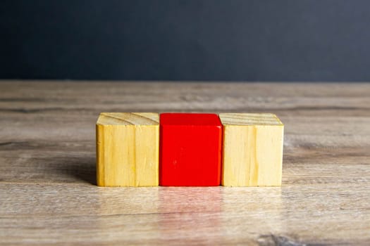 Three wooden cubes stand on a wooden table, two with which white one is red.