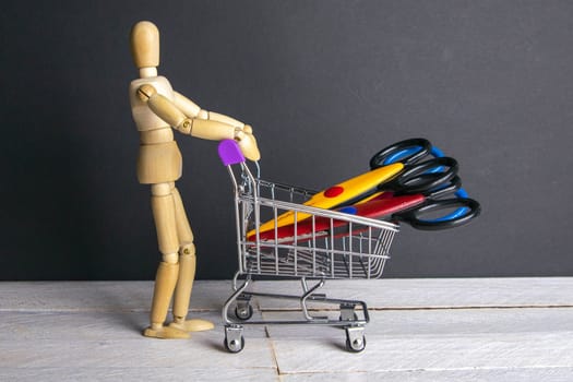 Shopping concept. Figure of a wooden man with a basket filled with stationery scissors.