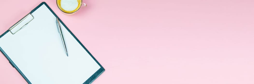 Tablet with a white sheet on which there is a silver pen and next to there is a glass with a coffe with milk.