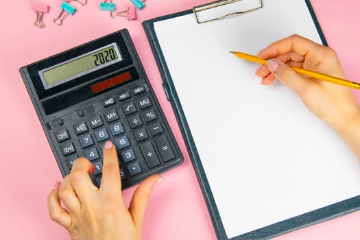 The hands of a woman count on a calculator and write notes. Top view of business woman's hands on white sheet. Finance and business concept.
