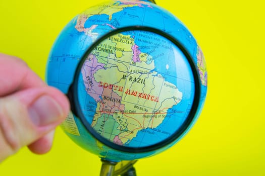 Close-up of a hand holding a magnifying glass to look at the globe in the library selective focus Brazil.