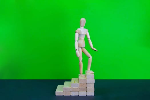 Wooden man walk up the career stairs. Ladder made with wooden bricks. Mannequin on top of development. Concept of personal development, career , changes, success. Green background, copy space for ad.
