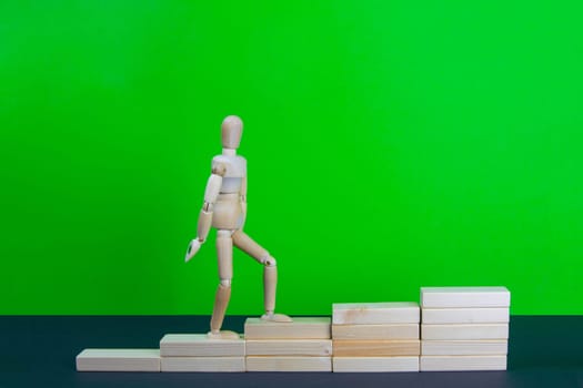 Wooden man walk up the career stairs. Ladder made with wooden bricks. Mannequin on top of development. Concept of personal development, career , changes, success. Green background, copy space for ad.
