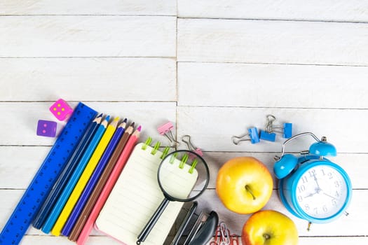 Various office stationery, notepad, clock, pencils, ooh, glasses, pen and two fresh apples on a white wooden table. Top view with copy space. Concept of office, education, workplace, school.