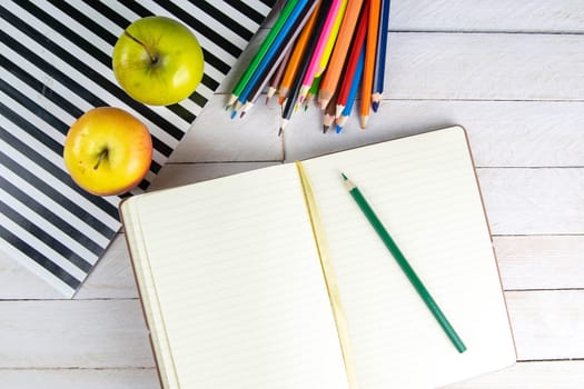 Top view of open notebook with empty pages, pencil and red apples on wooden table in office workspace.