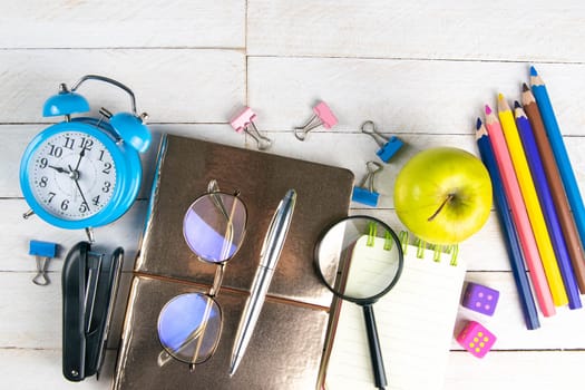 Various office stationery, notepad, clock, pencils, ooh, glasses, pen and two fresh apples on a white wooden table. Top view with copy space. Concept of office, education, workplace, school.