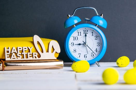 Easter concept, clock and apple, yellow books, eggs are scattered next to them, there is a wreath in the background.