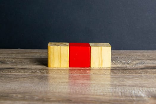Three wooden cubes stand on a wooden table, two with which white one is red.
