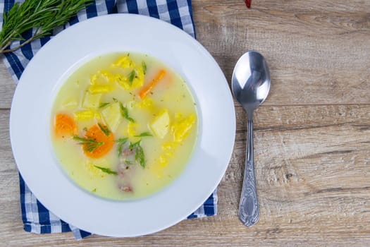 Potato cream soup with mushrooms, carrots and cheese. Top view. The plate stands on a checkered towel, next to a spoon.