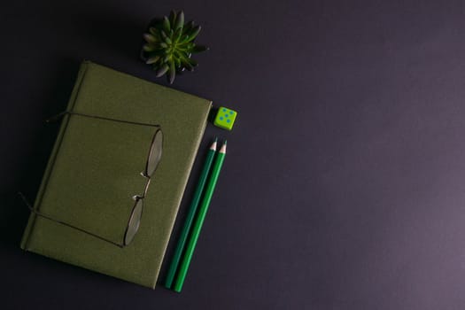 A green notebook with glasses on it has a green plant and green pencils next to the notebook.