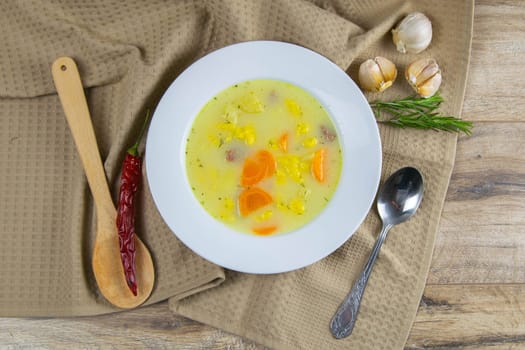 Potato cream soup with mushrooms, carrots and cheese. Top view. The plate is on a coffee towel, there is a spoon next to it.