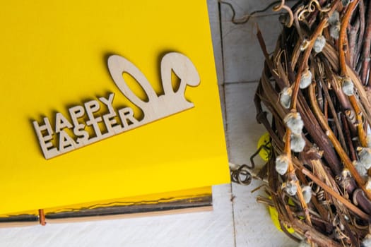 Easter concept. Yellow notepad with a sign of the sorly Easter and a wreath stand on a white wooden table.