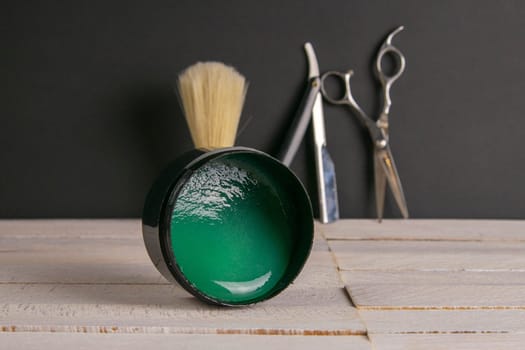 Dangerous razor and Scissors, gel for haircuts stand on a wooden table at a black wall. Concept of barber shop.