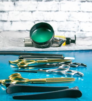 Hairdressing tools, scissors, hair clipper, comb, dangerous razor, hair gel stand on blue background.