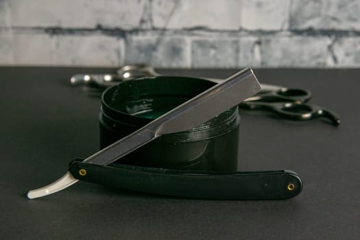 Dangerous razor and a gel for haircuts stand on a black table at a brick wall, the concept of barber shop.