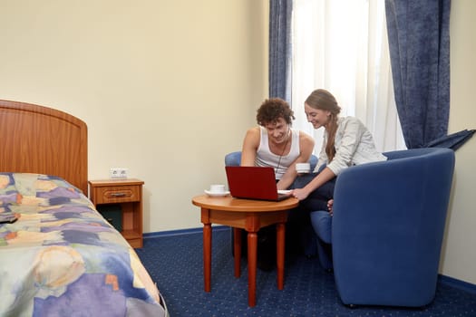 Happy young couple with laptop are sitting in armchair in living room at home. Internet communication. communication on network. Isolation period, quarantine, social distancing