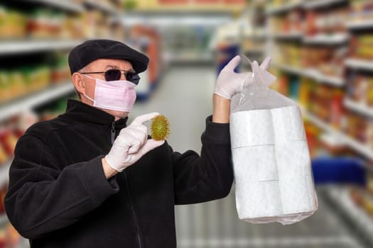 Coronavirus panic concept. Man with surgical mask, hood, glasses and medical gloves shows a package of toilet paper and an abstract model of a virus covid-19 over blurred super market background.