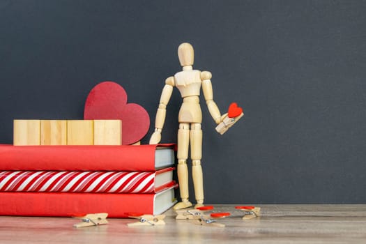 A stack of red books on which there are 4 wooden cubes, and next to there is a figure of a wooden man with a pin in the shape of a heart in his hand. Front views with clear space