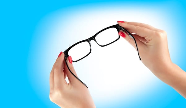 Female hand holding a black-framed glasses isolated on blue background