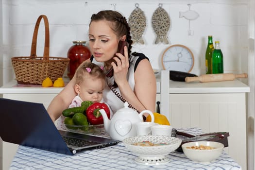 Mother with notebook and little child sit at dining table in home kitchen. Isolation period, quarantine, social distancing. Remote education or remote work