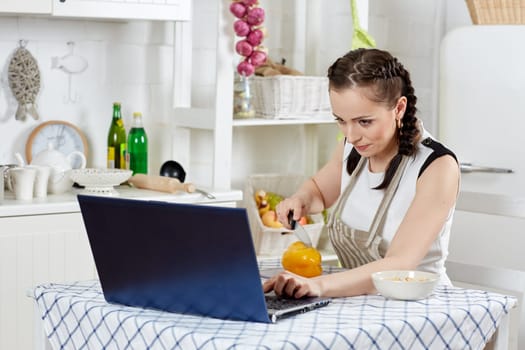 Woman in an apron with notebook  cooks in the kitchen. Isolation period, quarantine, social distancing. Remote education or remote work.