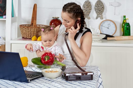 Mother with notebook and little child sit at dining table in home kitchen. Isolation period, quarantine, social distancing. Remote education or remote work