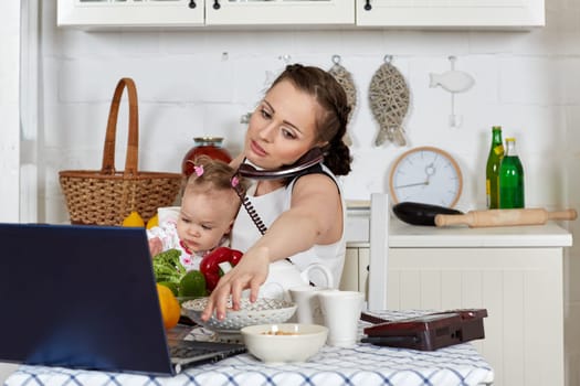 Mother with notebook and little child sit at dining table in home kitchen. Isolation period, quarantine, social distancing. Remote education or remote work