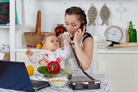 Mother with notebook and little child sit at dining table in home kitchen. Isolation period, quarantine, social distancing. Remote education or remote work