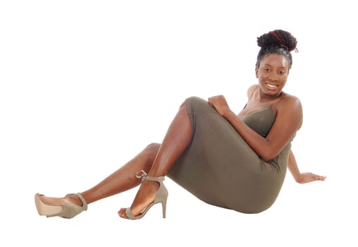 A beautiful African American woman in a dress sitting on.the floor, smiling, isolated for white background.