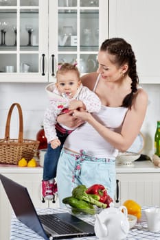 Young mother feeds little daughter  in the home kitchen. Happy family.