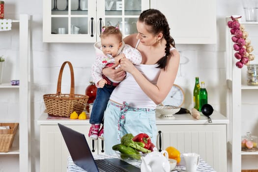 Young mother feeds little daughter  in the home kitchen. Happy family.