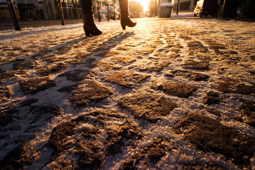 Pavement with cobblestones in winter snow and female legs