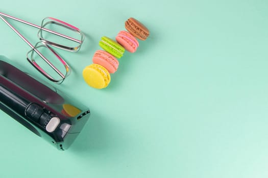 Colorful macaroons and mixer on mint background. Top views with clear space.