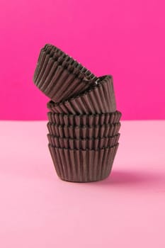 Pinc background with brown paper forms for muffins. Close-up.