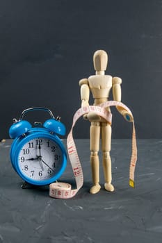 Wood Figure Mannequin with measuring tape and blue clock, dieting Concept. Close-up