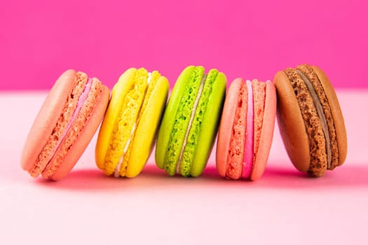 Colorful macaroons stand in a row against a pink background. Close-up