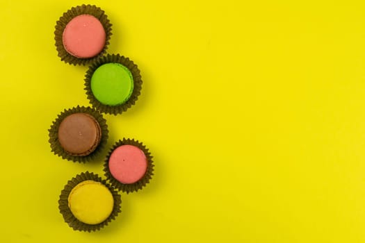 Colorful macaroons in a beautiful brown wrapper stand on a yellow background. Top views with clear space