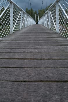 Low view of the bridge. Wood paved and white fence bounded by a suspension bridge in the Donja Dubrava. The bridge is the last building at the Donja Dubrava hydroelectric power plant. The gloomy weather and low view seem to be the starting point of a long journey.