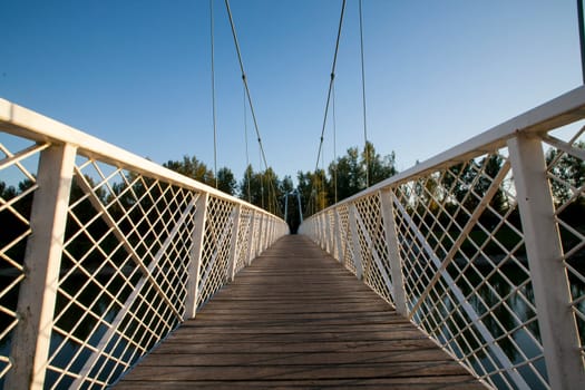 Bridge in Donja Dubrava, Croatia. Hanging white bridge with wooden tread. Low POV. Attractive bridge for recreation and walking because it connects part of the city with nature and the river Drava.