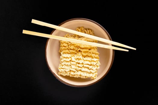 Instant noodles with wood sticks. Asian fast food on a black background close-up. Top views.