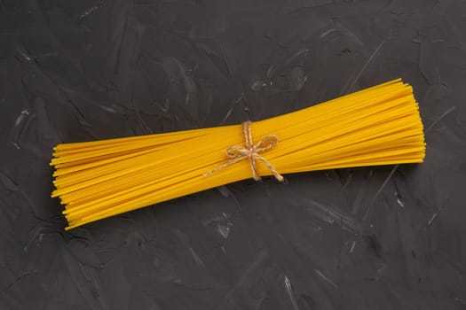 Yellow long spaghetti bound by a bagve on a dark background. Top views.