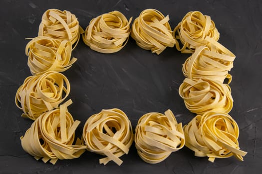 Raw tagliatelle pasta noodles frame and border isolated on black background, top view with clear space