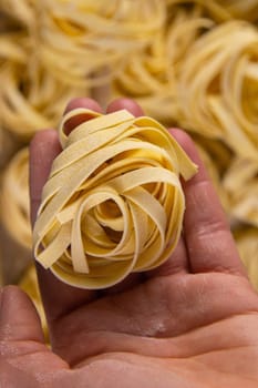 Homemade italian pasta. Woman's hand holds tagliatelle over the background of the pasta tagliatelle background. Top views.