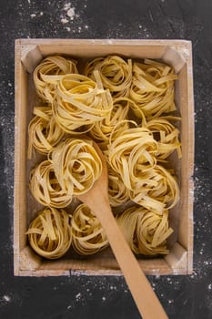 Still life of preparing pasta on rustic wooden background. Raw tagliatelle in a wooden box with wooden spoon. Top views.