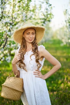 The beautiful girl the blonde in the blossoming apple-trees garden. White flowers in a garden in sunshine. Spring apple trees in blossom. Beautiful woman among spring blossom