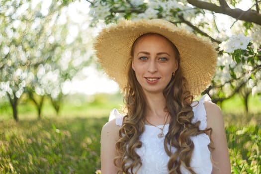 The beautiful girl the blonde in the blossoming apple-trees garden. White flowers in a garden in sunshine. Spring apple trees in blossom. Beautiful woman among spring blossom