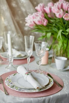 Decor and spring table setting is a vase with pink tulips and dishes of white color. Selective focus.
